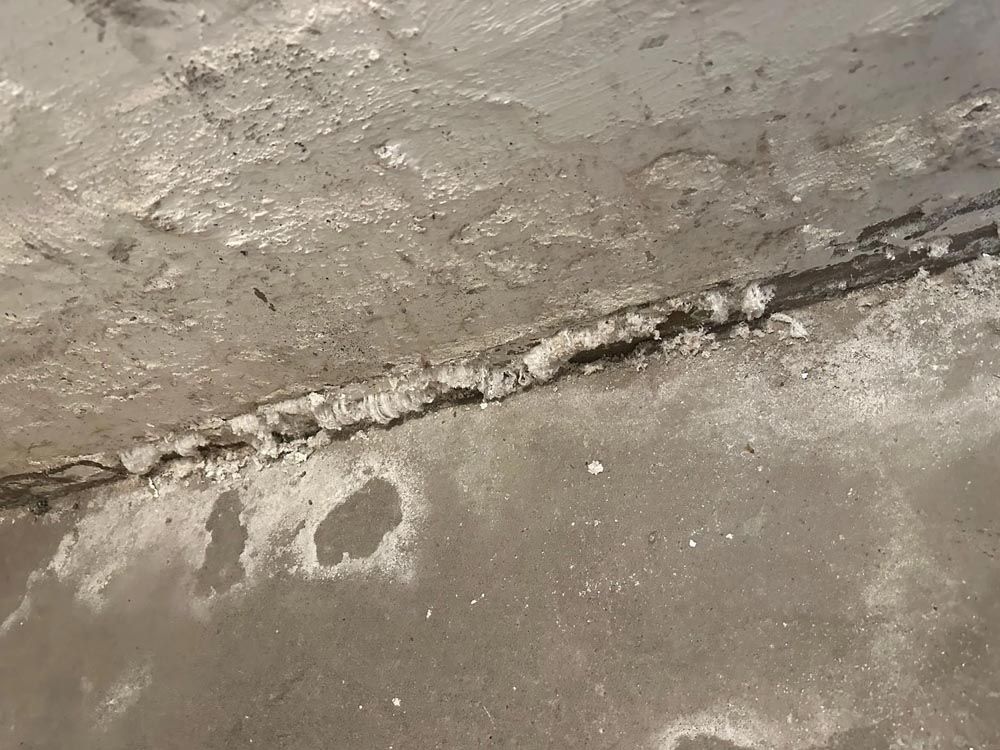 Betonboden mit einem Riss, der mit weißen, kristallinen Ablagerungen gefüllt ist.