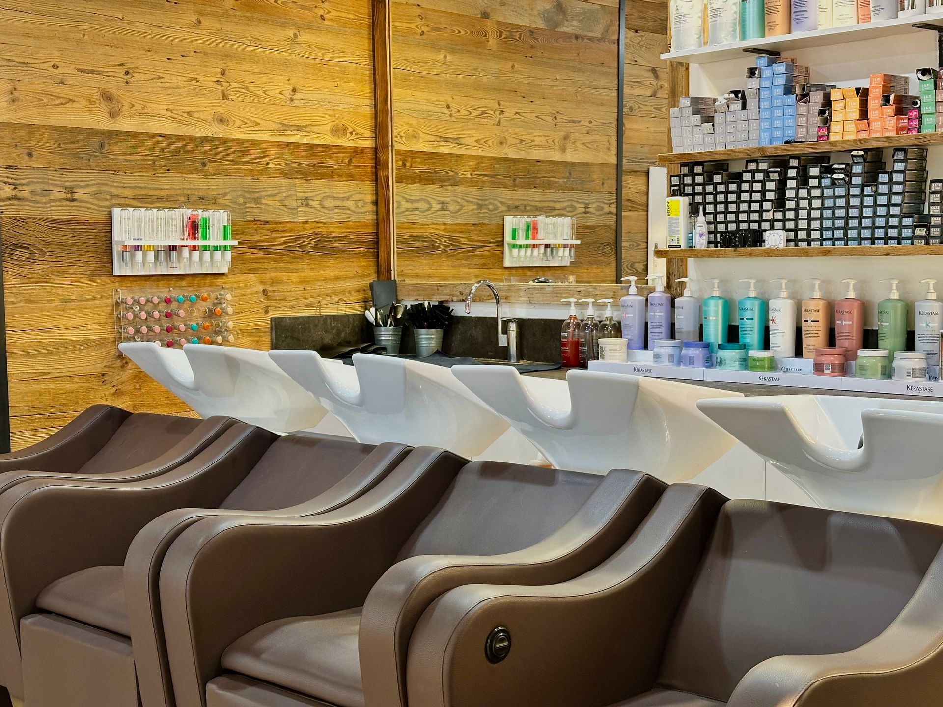 Espaces de shampoing avec chaises marron et lavabos blancs à côté d'étagères de produits capillaires