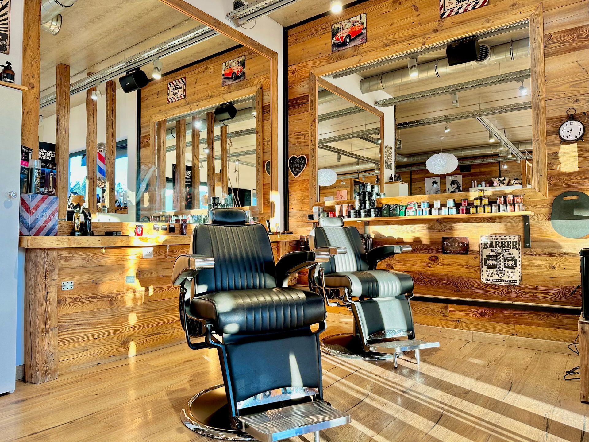 Intérieur d'un salon de coiffure avec fauteuils en cuir noir, grands miroirs, décoration en bois et sols cirés
