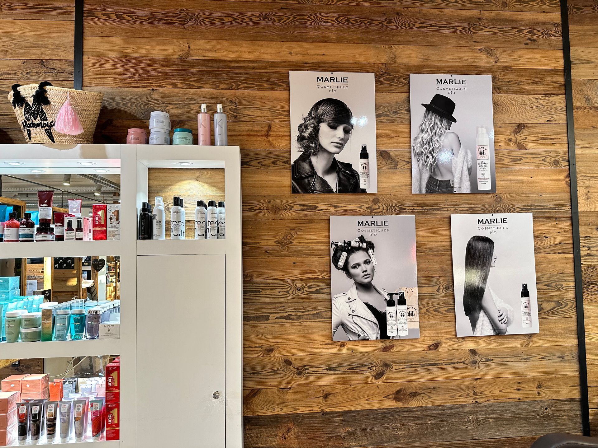 Mur d'un salon de beauté avec des posters de coiffures au-dessus des étagères à produits et une armoire blanche