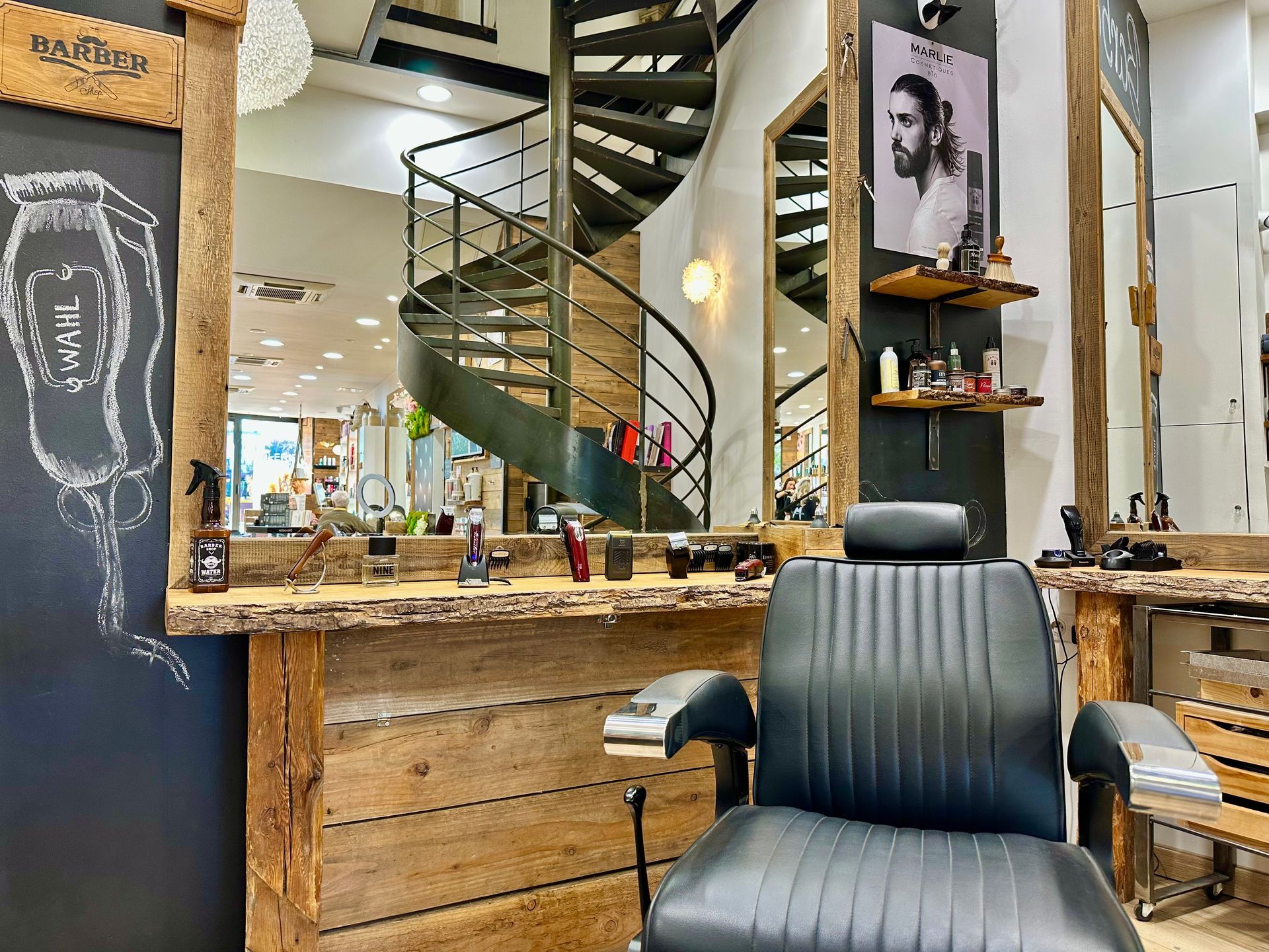 Salon de coiffure moderne avec un fauteuil noir, des comptoirs en bois et un escalier en colimaçon en arrière-plan.