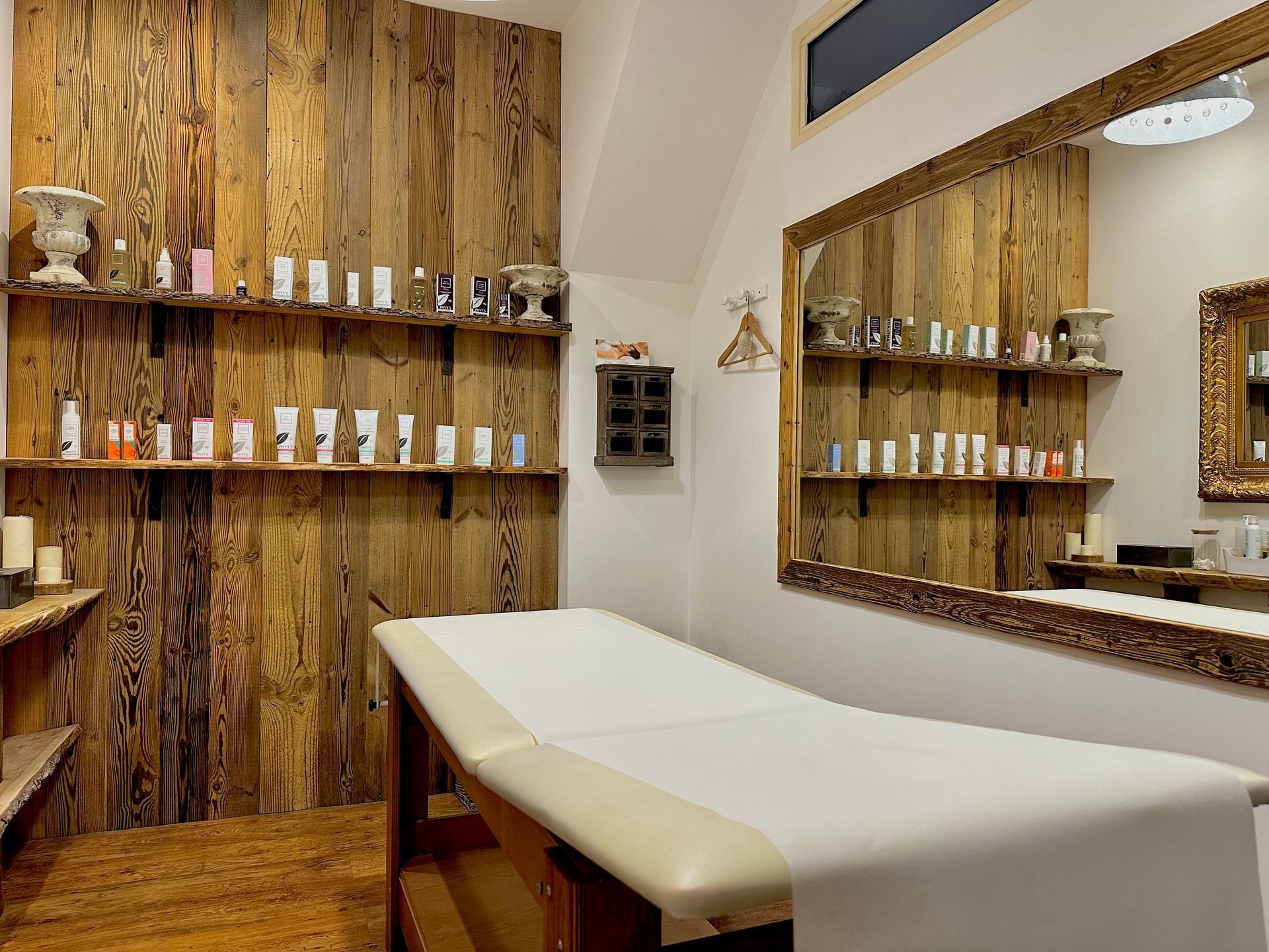 Salle de soins avec table de massage, murs lambrissés, étagères de flacons et grand miroir.