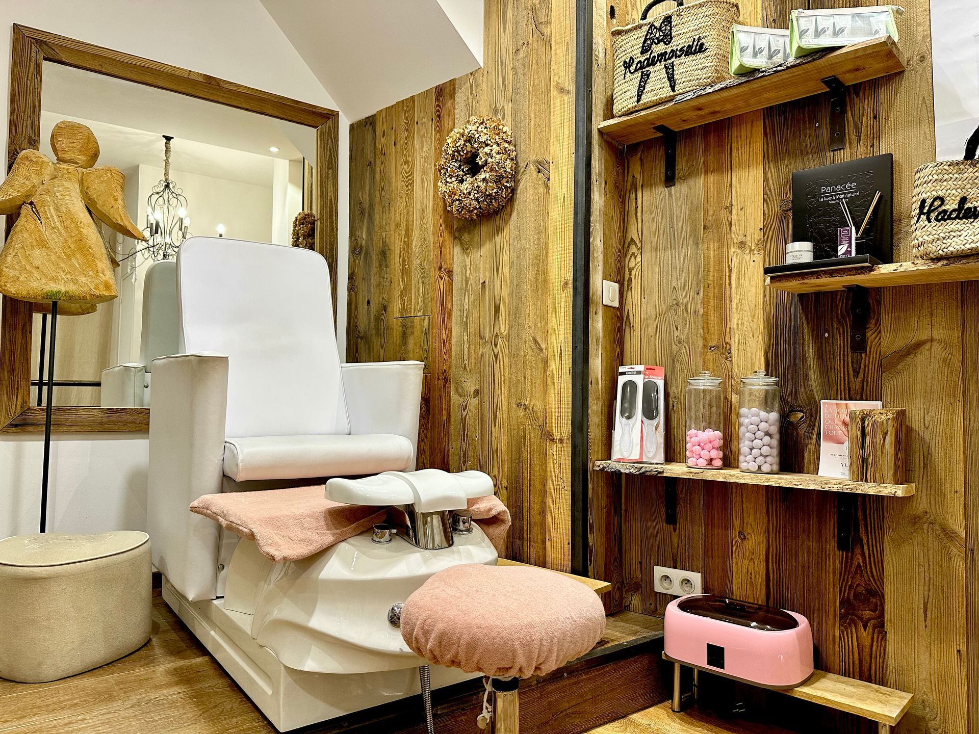 Salon cosy avec un fauteuil de pédicure blanc, des étagères en bois et des touches de rose.