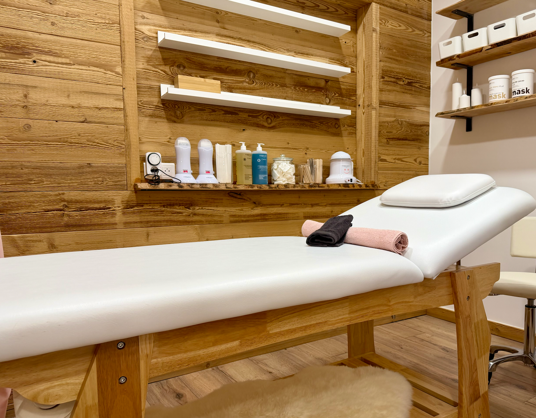 Salle de massage lambrissée avec table de massage, étagères de produits et serviettes roulées