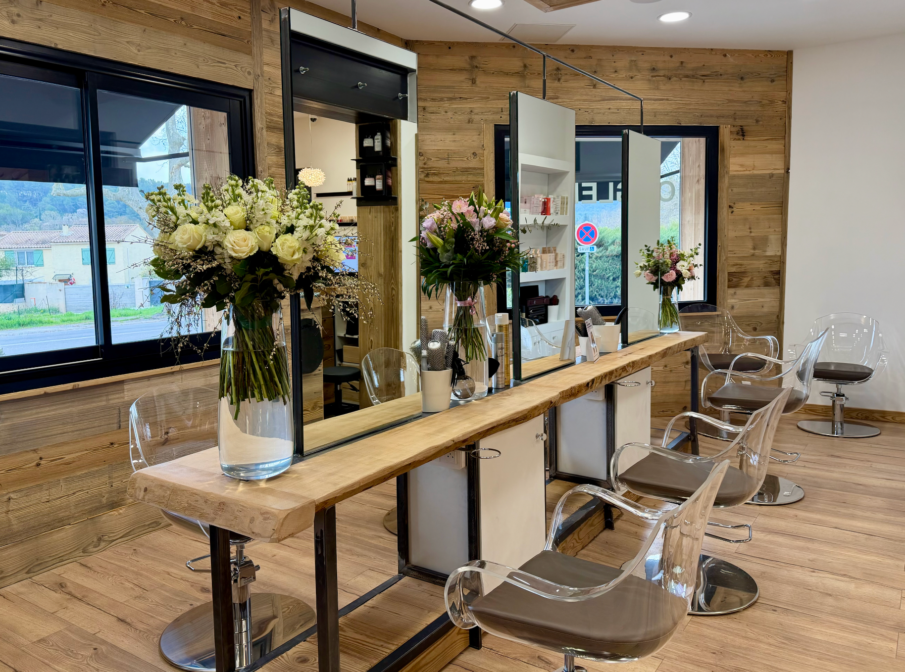 Salon moderne avec fauteuils de coiffure, miroirs et compositions florales dans un intérieur lumineux lambrissé.