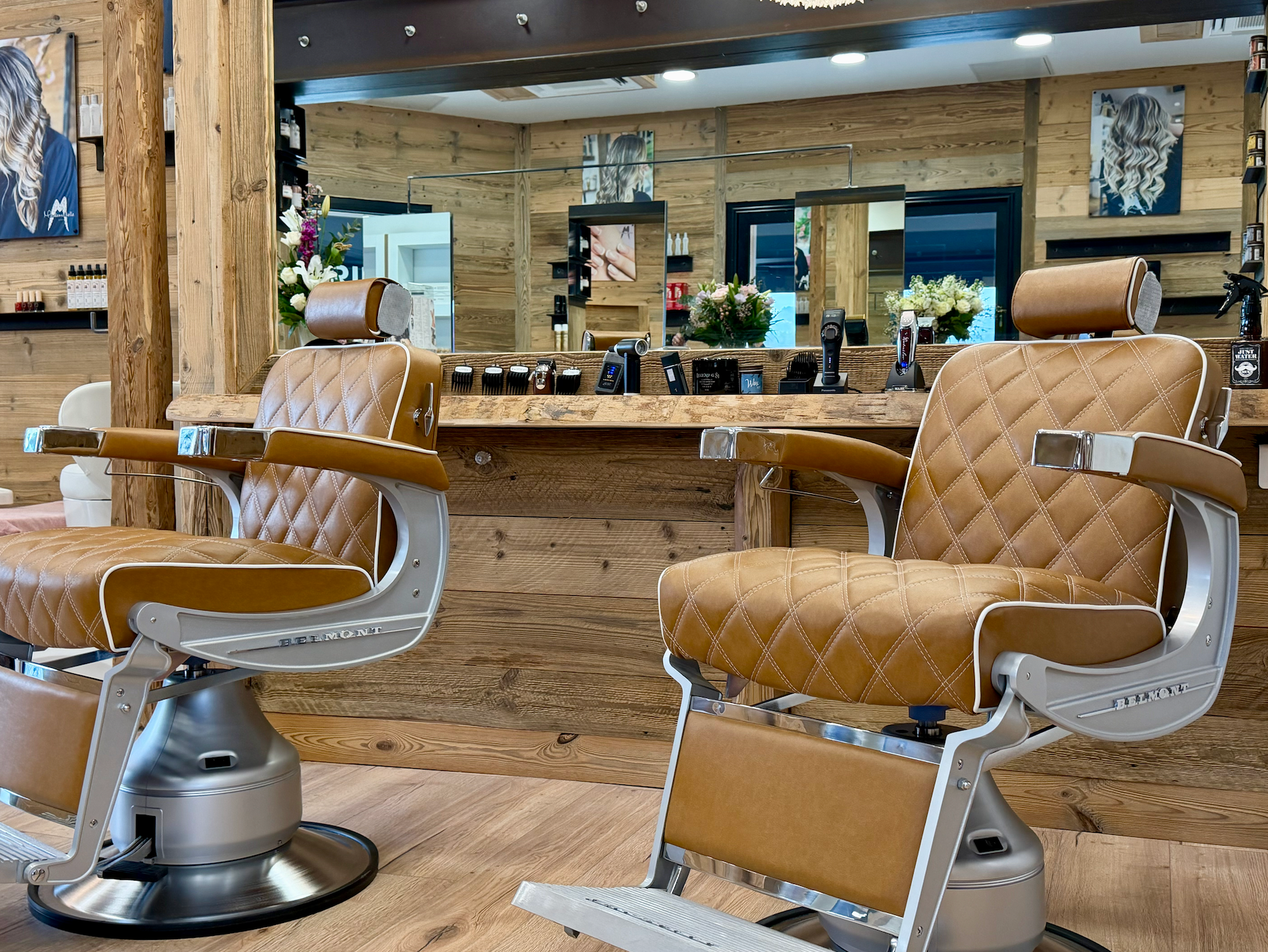 Salon de coiffure avec deux fauteuils en cuir beige face à un miroir et un comptoir en bois.