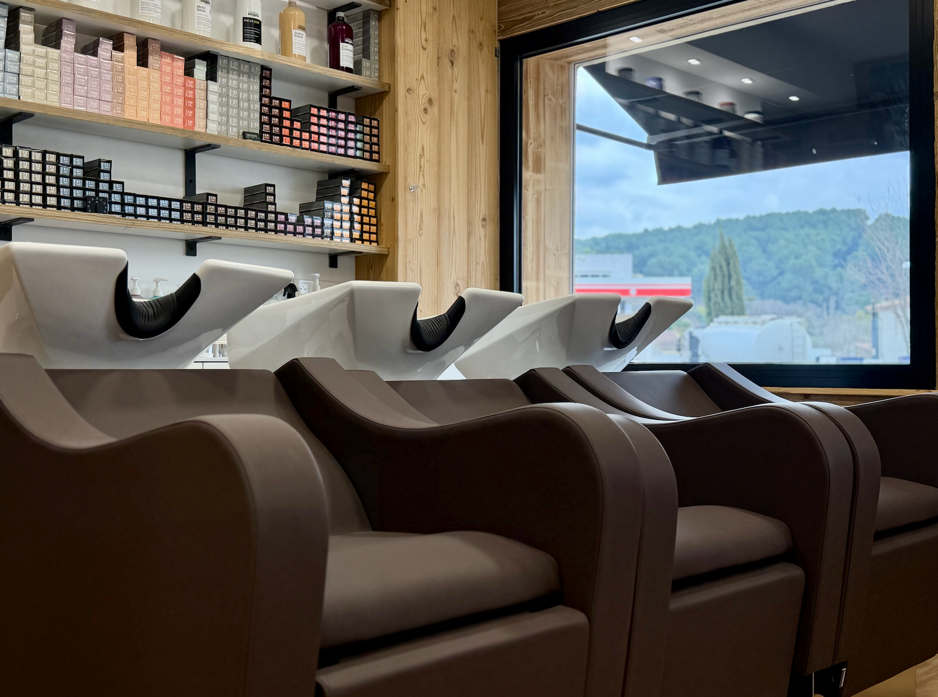 Des fauteuils de lavage de cheveux de salon près d'une fenêtre, avec des étagères de produits capillaires