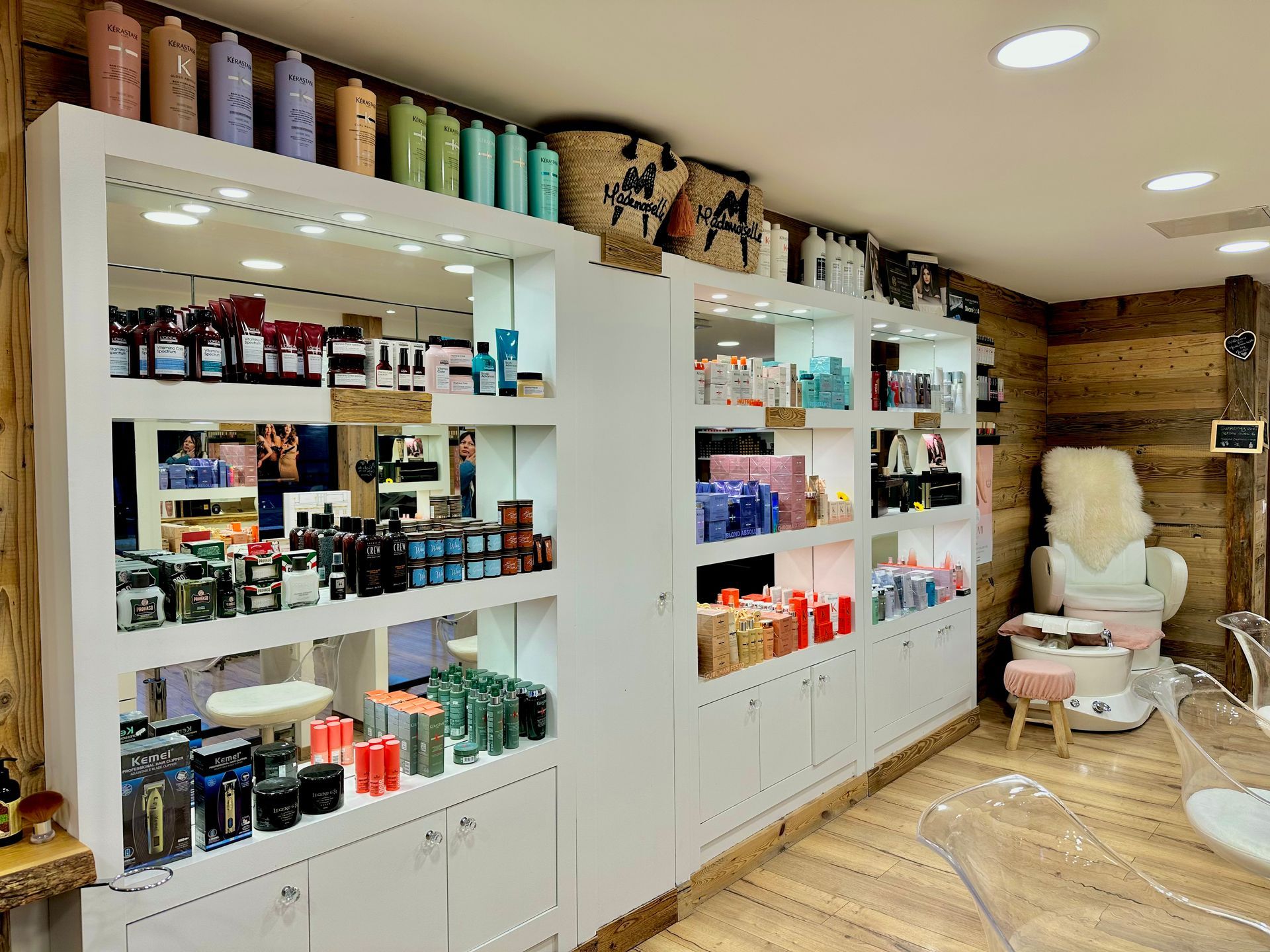 Des étagères remplies de produits capillaires, côtoient un fauteuil de coiffure blanc et un miroir.