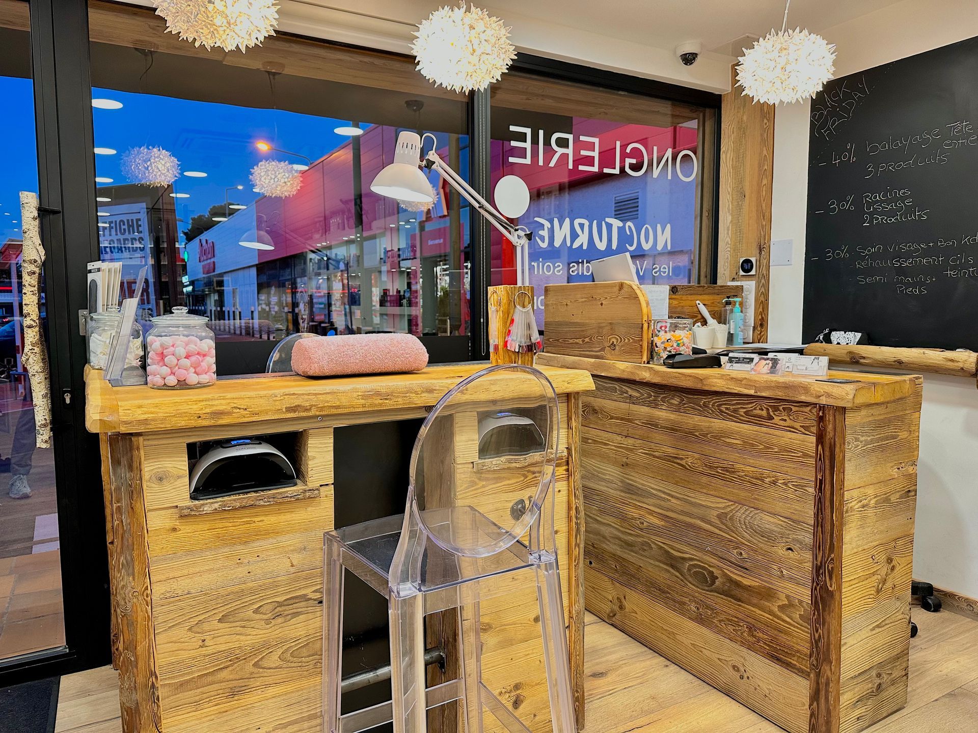 Comptoir lumineux d'un espace manucure, avec des lampes et une chaise transparente près d'une vitrine.