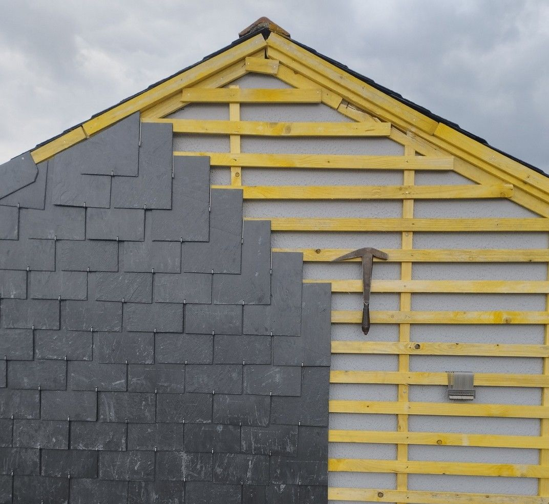 Toiture partiellement recouverte de bardeaux d'ardoise gris foncé ; bruit de marteau sur le mur.