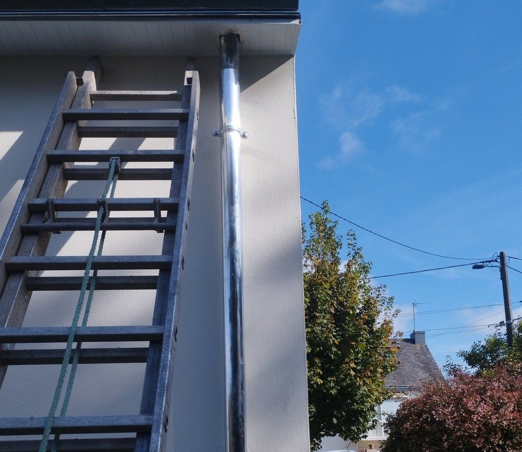 Une échelle est appuyée contre un bâtiment blanc avec une descente de gouttière argentée. Ciel d'un bleu éclatant.