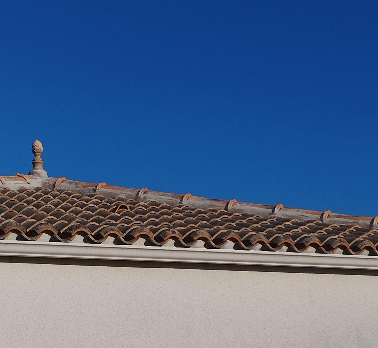 Toit de tuiles en terre cuite se détachant sur un ciel d'un bleu profond. Façade d'un bâtiment couleur crème.