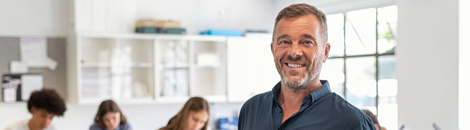 Lächelnder Mann im blauen Hemd in einem Klassenzimmer mit Schülern.