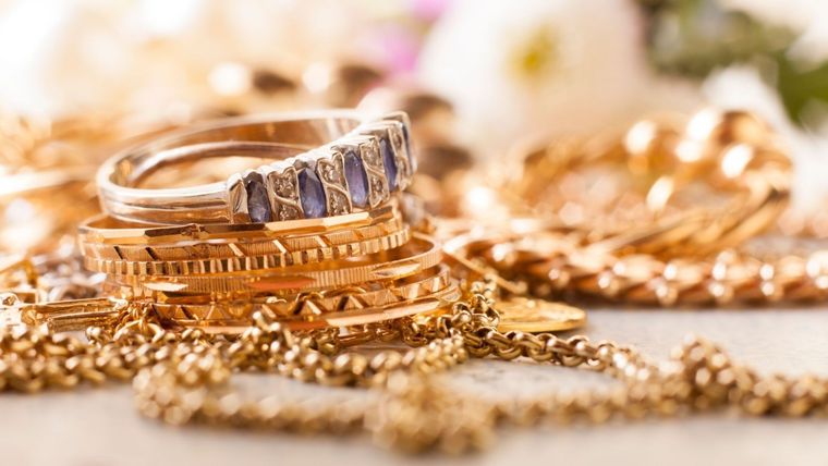 Una pila de joyas de oro que incluye un anillo y pulseras sobre una mesa.