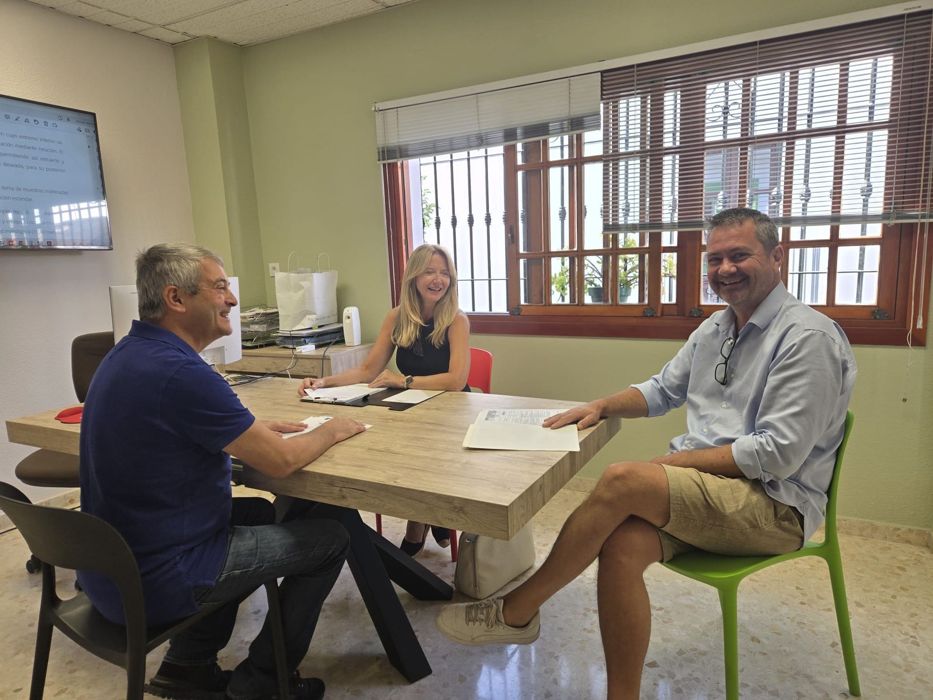 Tres personas sentadas en una mesa en una oficina, discutiendo papeleo.