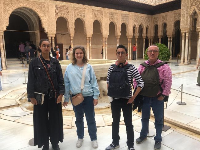 Cuatro personas posan en un patio ornamentado con arcos y una fuente central.