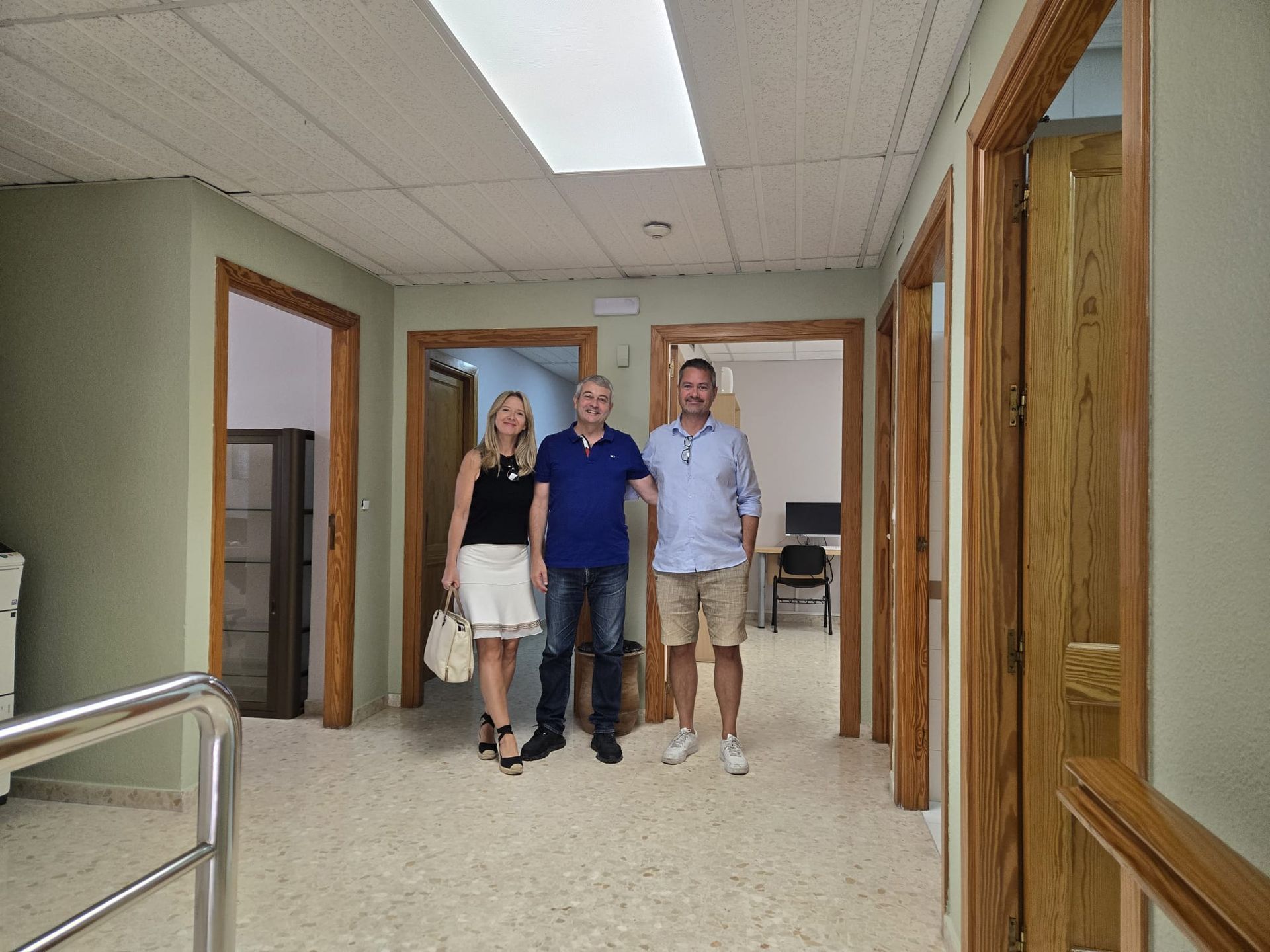 Tres personas están de pie en un pasillo con las puertas abiertas. Las paredes están pintadas de verde y el suelo es beige.