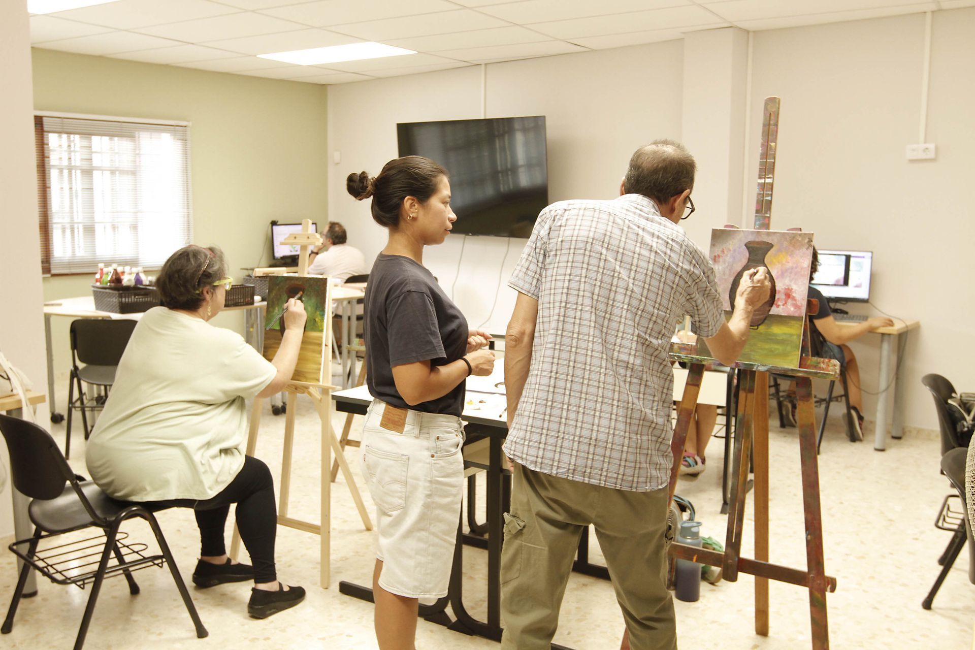 Personas pintando en clase de arte; el instructor ayuda a un estudiante. Interior.