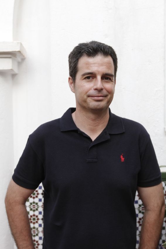 Una mujer con una sudadera con capucha de color burdeos sonríe frente a la vegetación.