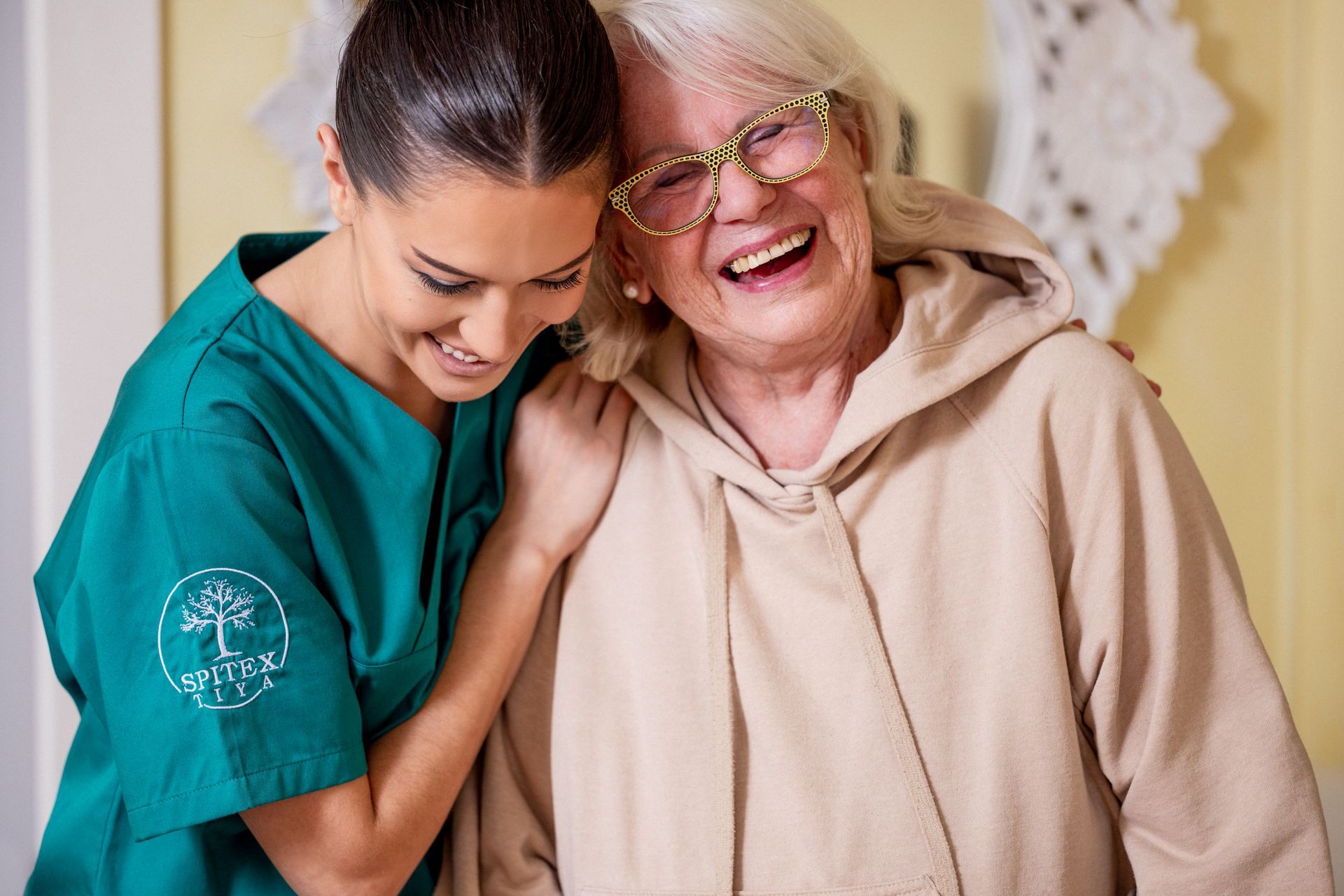 Eine ältere Frau hält die Hand einer Krankenschwester, während sie auf einer Couch sitzt. Spitex Tiya GmbH