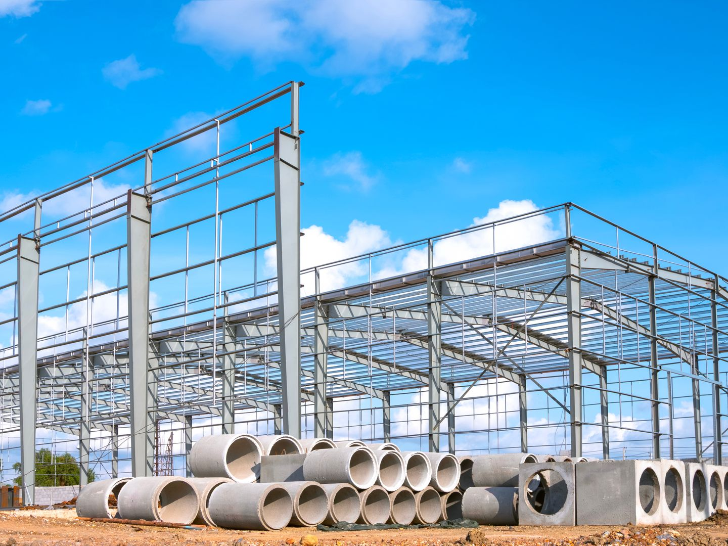 Structure métallique d'un bâtiment en construction, avec des tuyaux en béton devant.