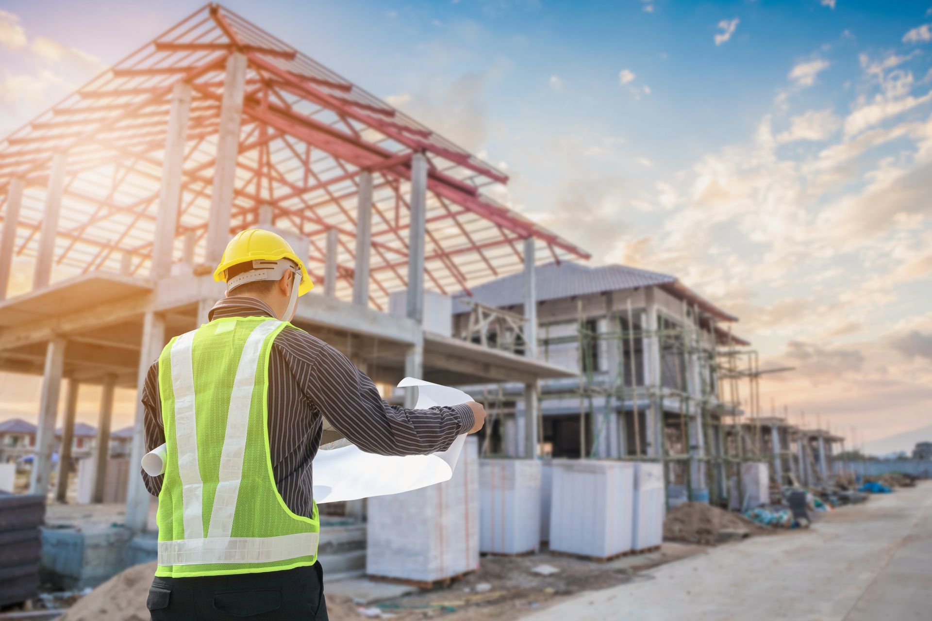 Un ouvrier du bâtiment, portant un casque et un gilet jaune, examine des plans sur un chantier de construction de maisons.