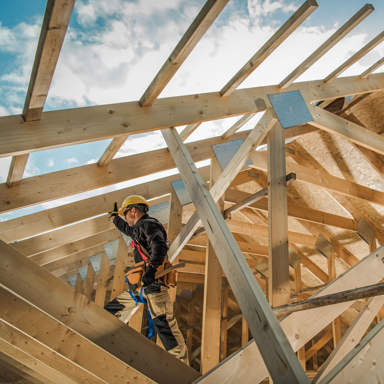 Ouvrier du bâtiment portant un casque de chantier, sur la charpente d'un toit.