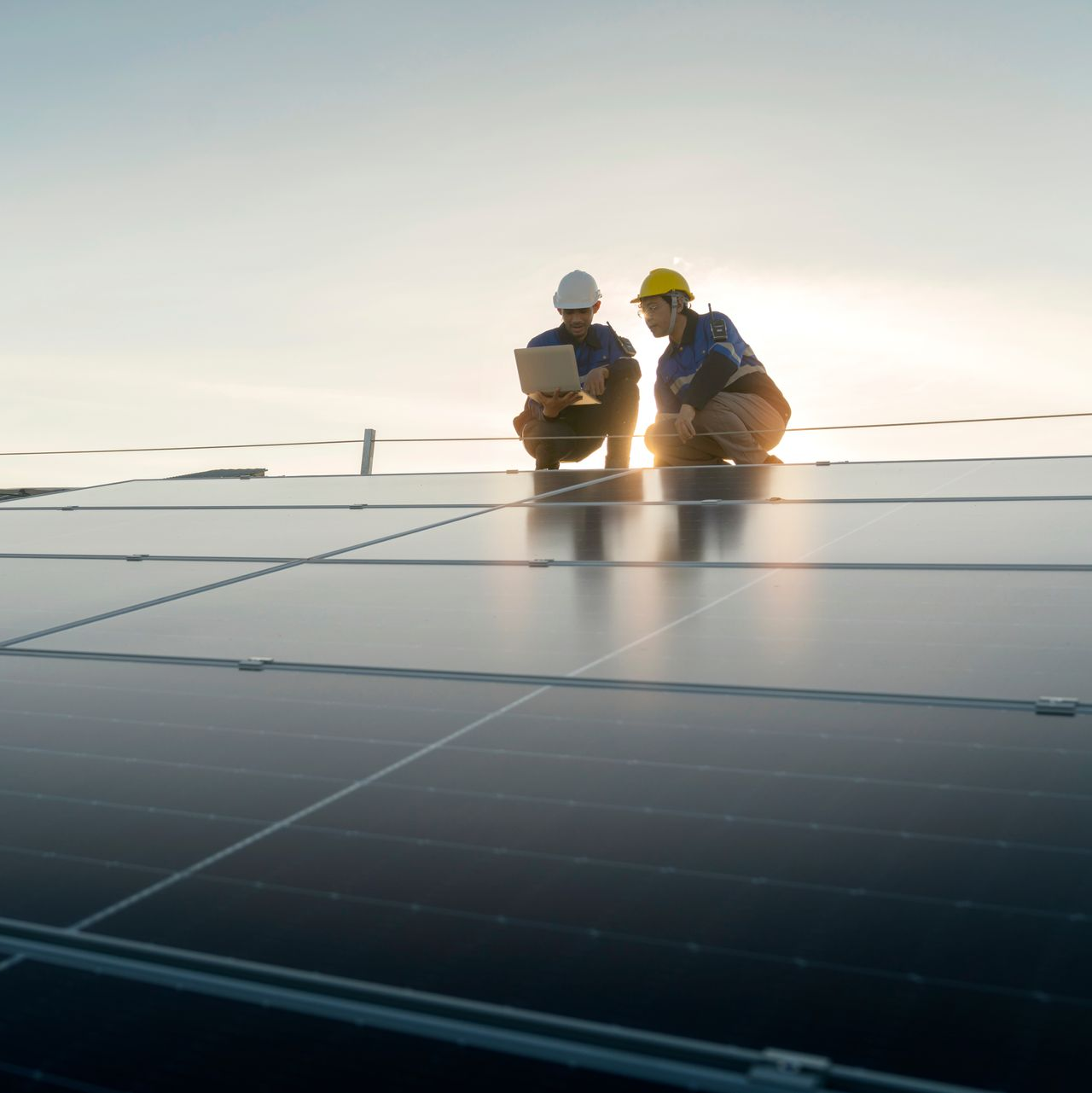 Deux ouvriers inspectent des panneaux solaires sur un toit, à l'aide d'un ordinateur portable.