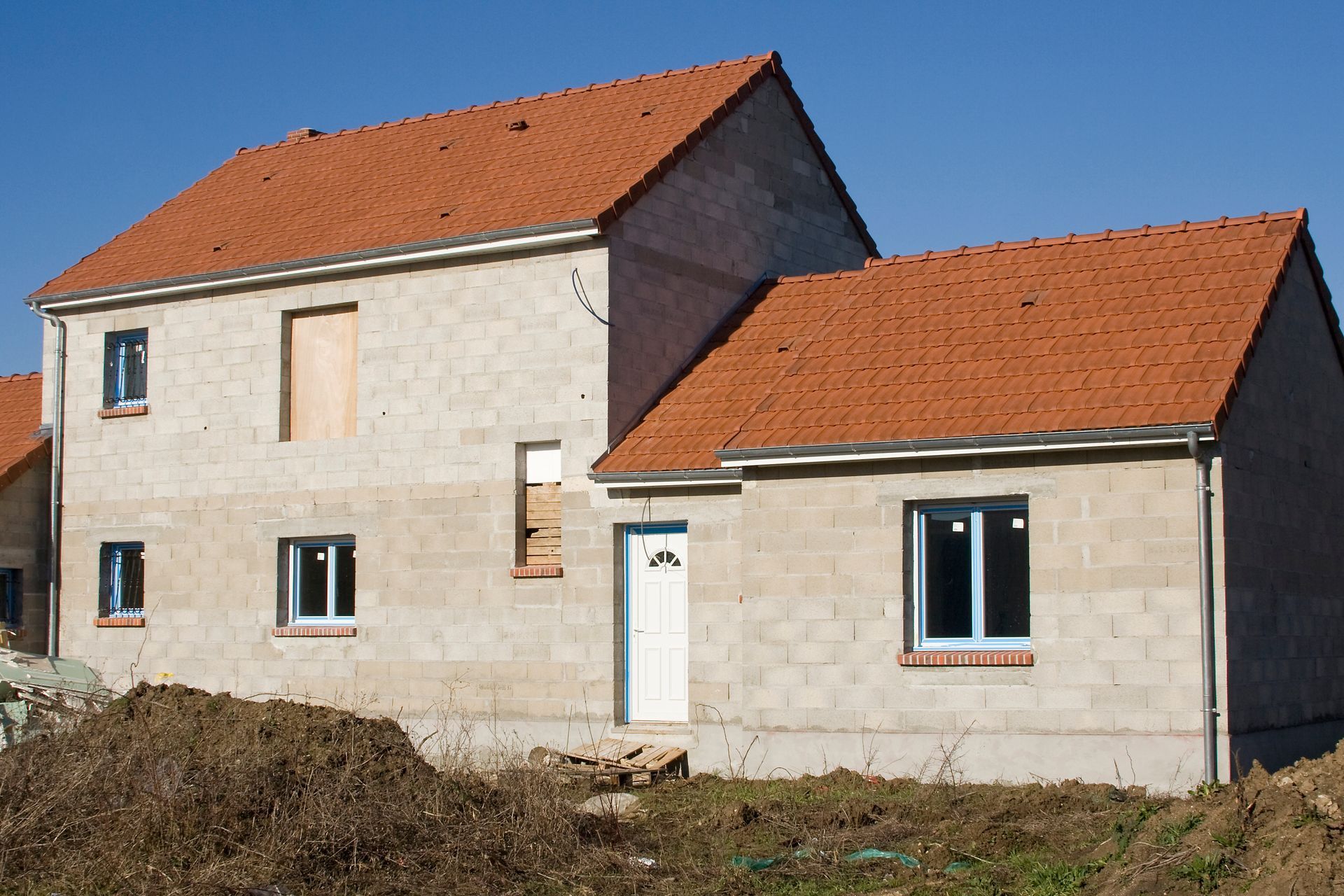 Maison à deux étages en construction, avec un toit de tuiles rouges et des murs en parpaings.