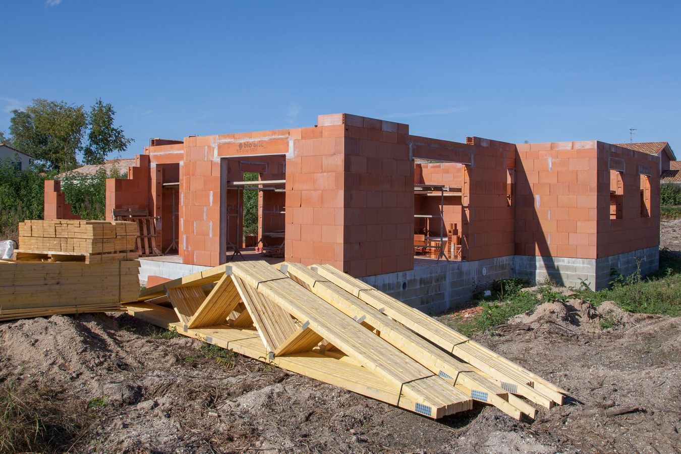 Chantier de construction d'une maison aux murs de briques rouges, à la charpente en bois.