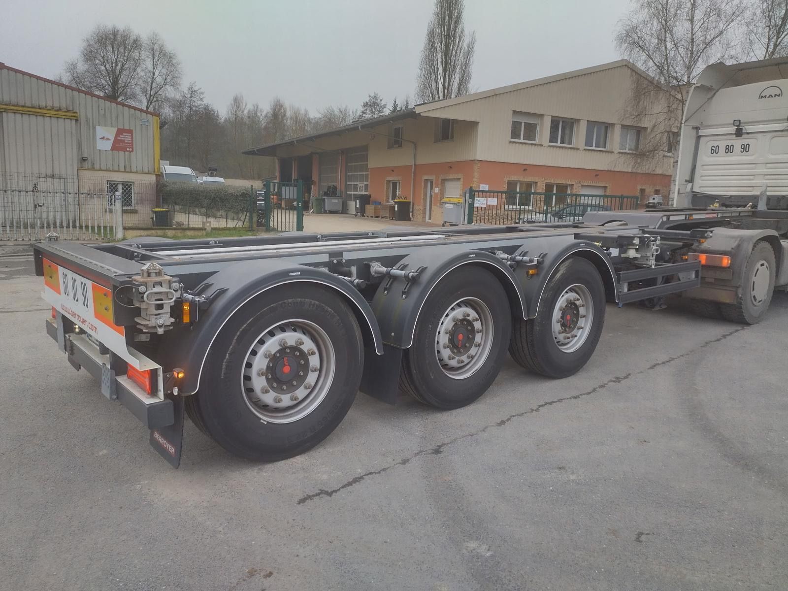 Semi-remorque plateau noire à trois essieux stationnée dans une rue industrielle détrempée, près de bâtiments