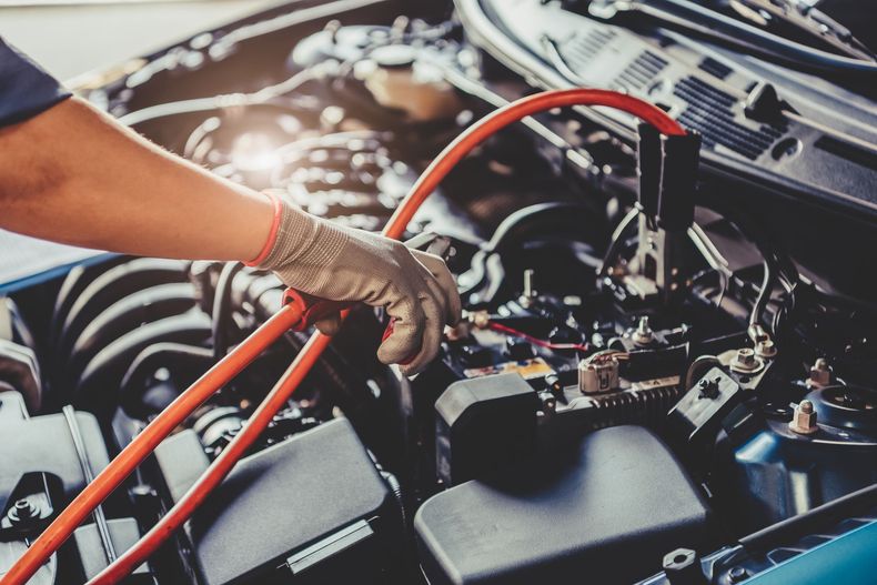 Main gantée travaillant sur le moteur de la voiture avec des câbles de démarrage rouges branchés à la batterie