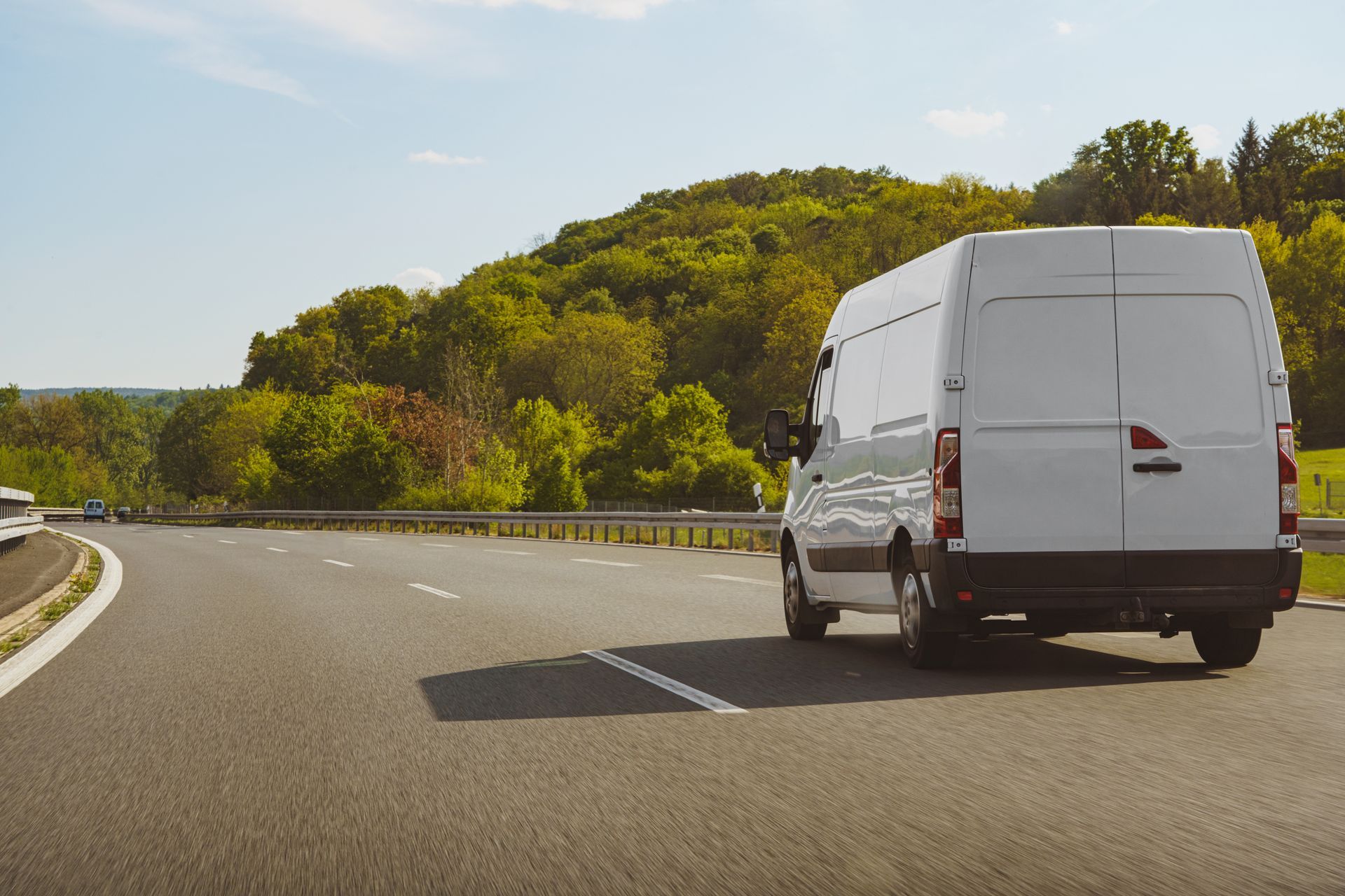 Une camionnette blanche roule sur une route sinueuse bordée de collines verdoyantes sous un ciel dégagé.
