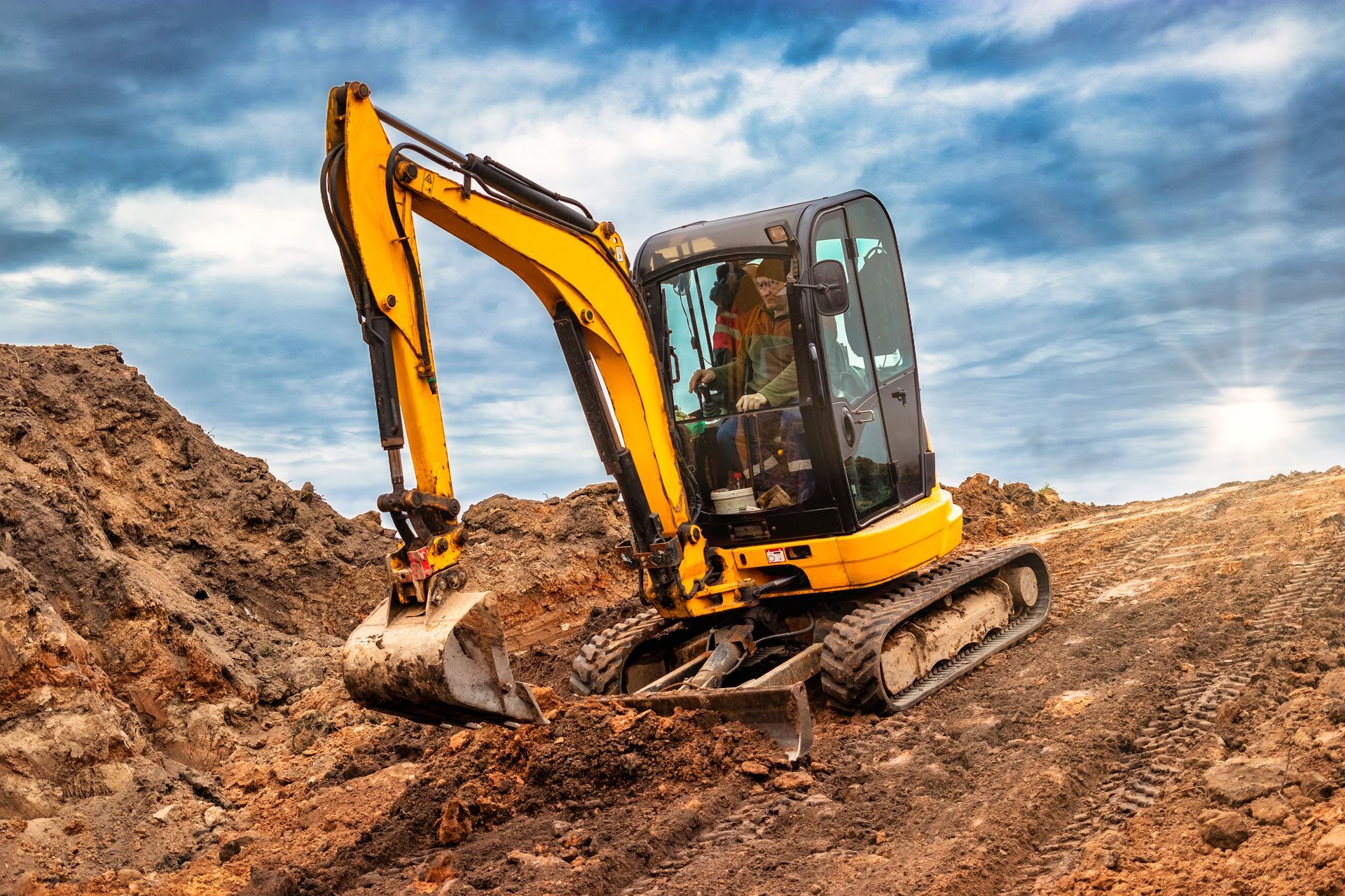 Une pelleteuse jaune travaille sur un chantier de construction en terre sous un ciel nuageux