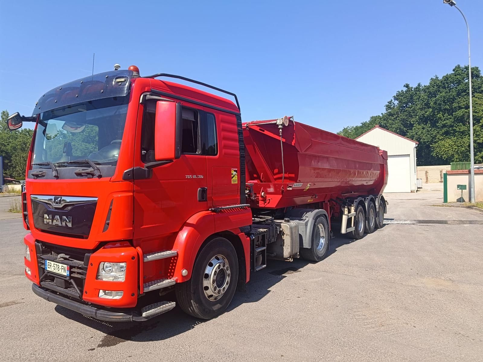 Un camion-benne rouge garé sur un terrain goudronné sous un ciel bleu dégagé