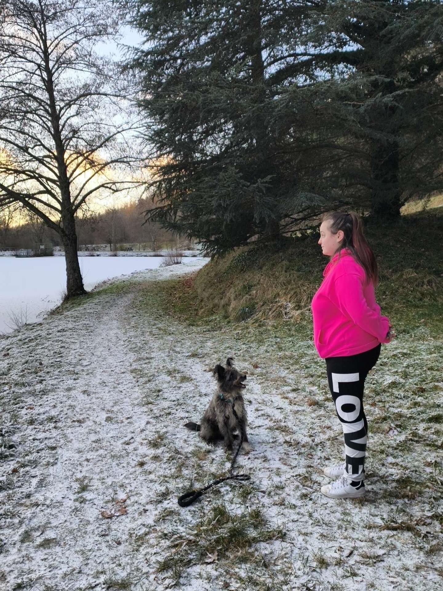 Une femme en veste rose et leggings entraîne un chien dans la neige.
