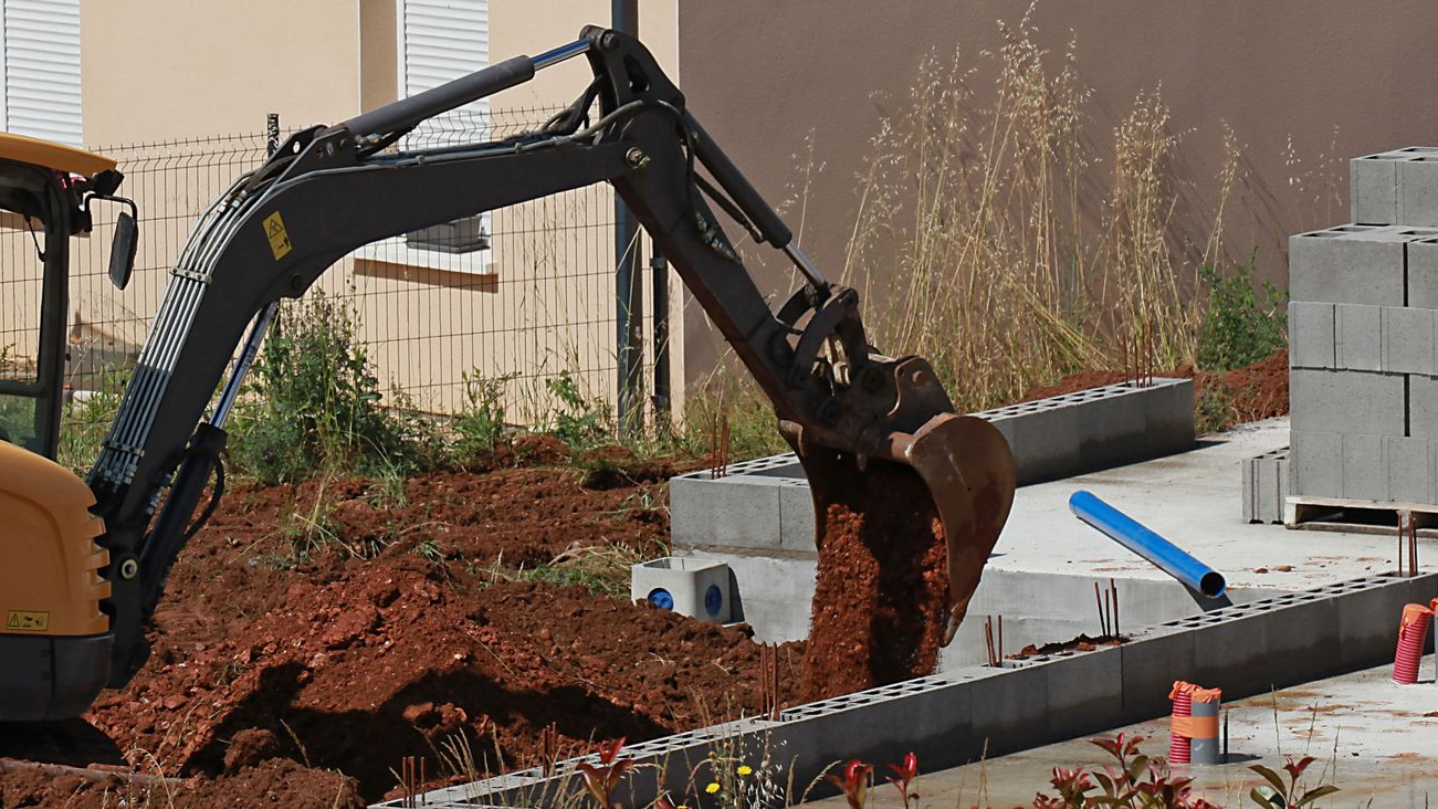 Une excavatrice creuse la terre à côté de blocs de béton sur un chantier de construction.