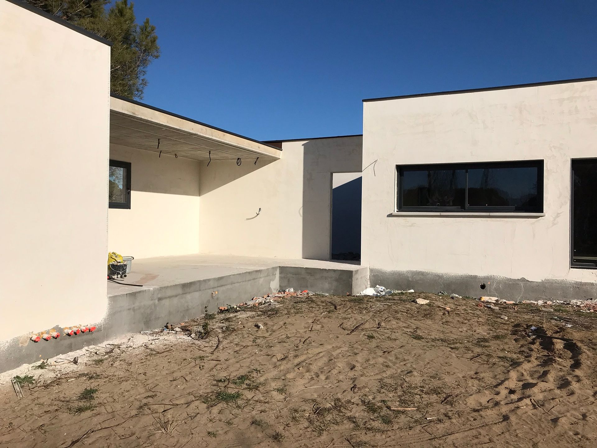 Maison blanche moderne avec une cour avant boueuse et un ciel bleu