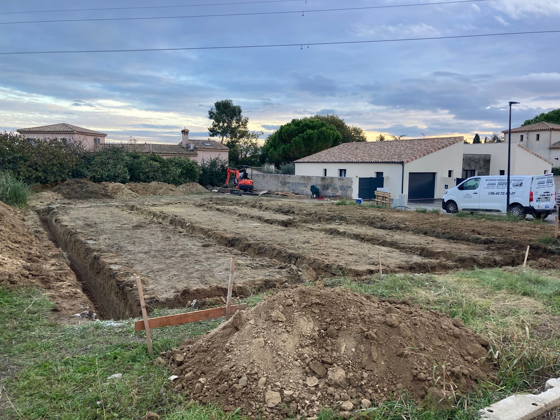 Chantier de construction avec des tas de terre et une petite excavatrice près des maisons au crépuscule