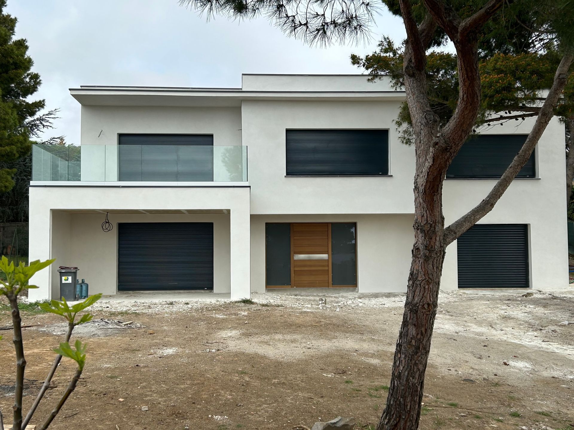 Maison moderne blanche de deux étages avec de grandes fenêtres sombres et un arbre dans la cour avant