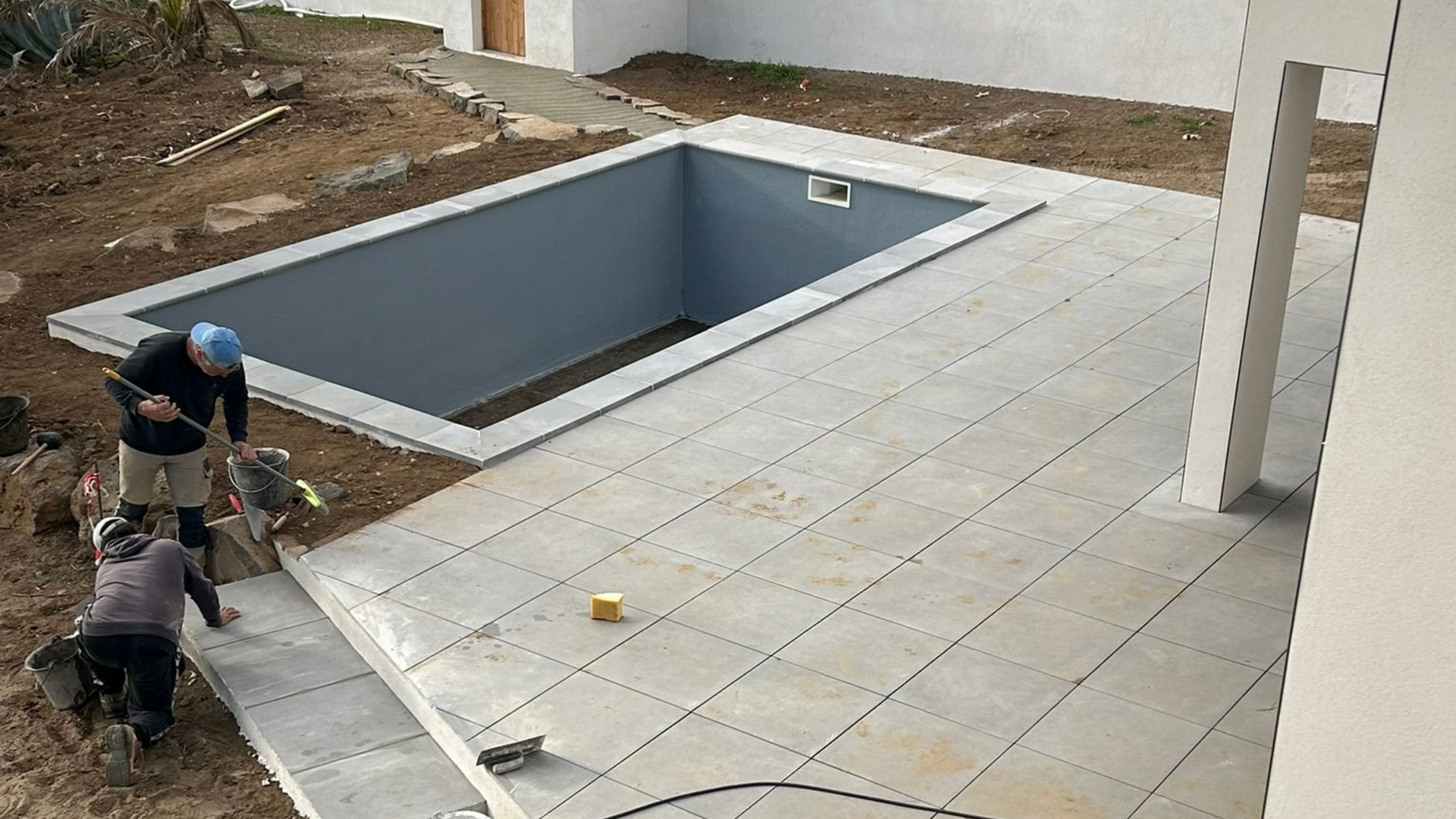 Des ouvriers posent du carrelage au bord d'une piscine creusée sur une terrasse en construction