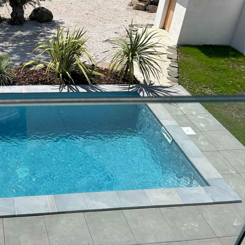 Piscine à l'arrière avec eau bleue, terrasse en carrelage gris et petits aménagements paysagers à proximité