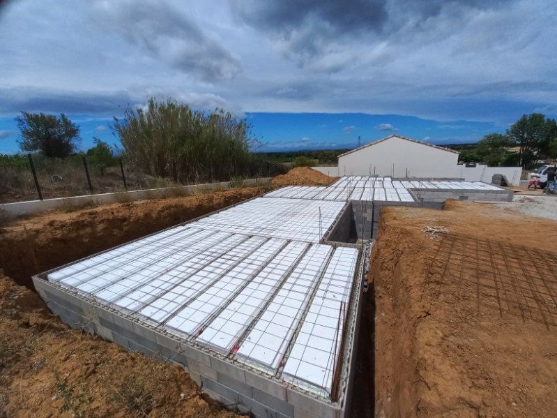 Chantier de construction avec des blocs blancs empilés et un long bâtiment blanc sous un ciel bleu nuageux