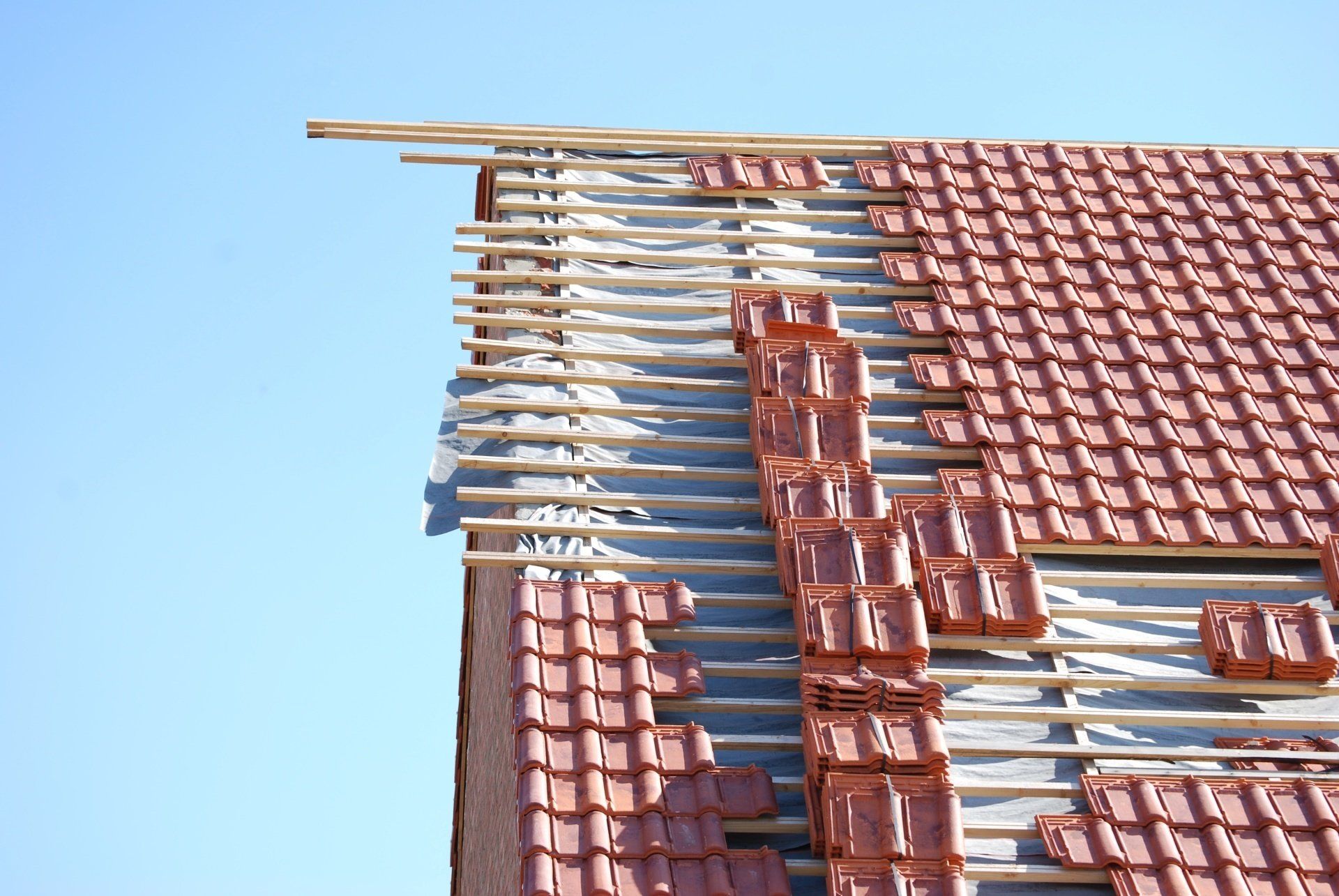 Toit de maison en tuiles rouges endommagé, avec des lattes de bois apparentes sur un ciel bleu