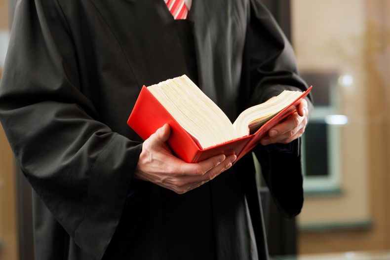 Personne en robe noire tenant un livre rouge ouvert.