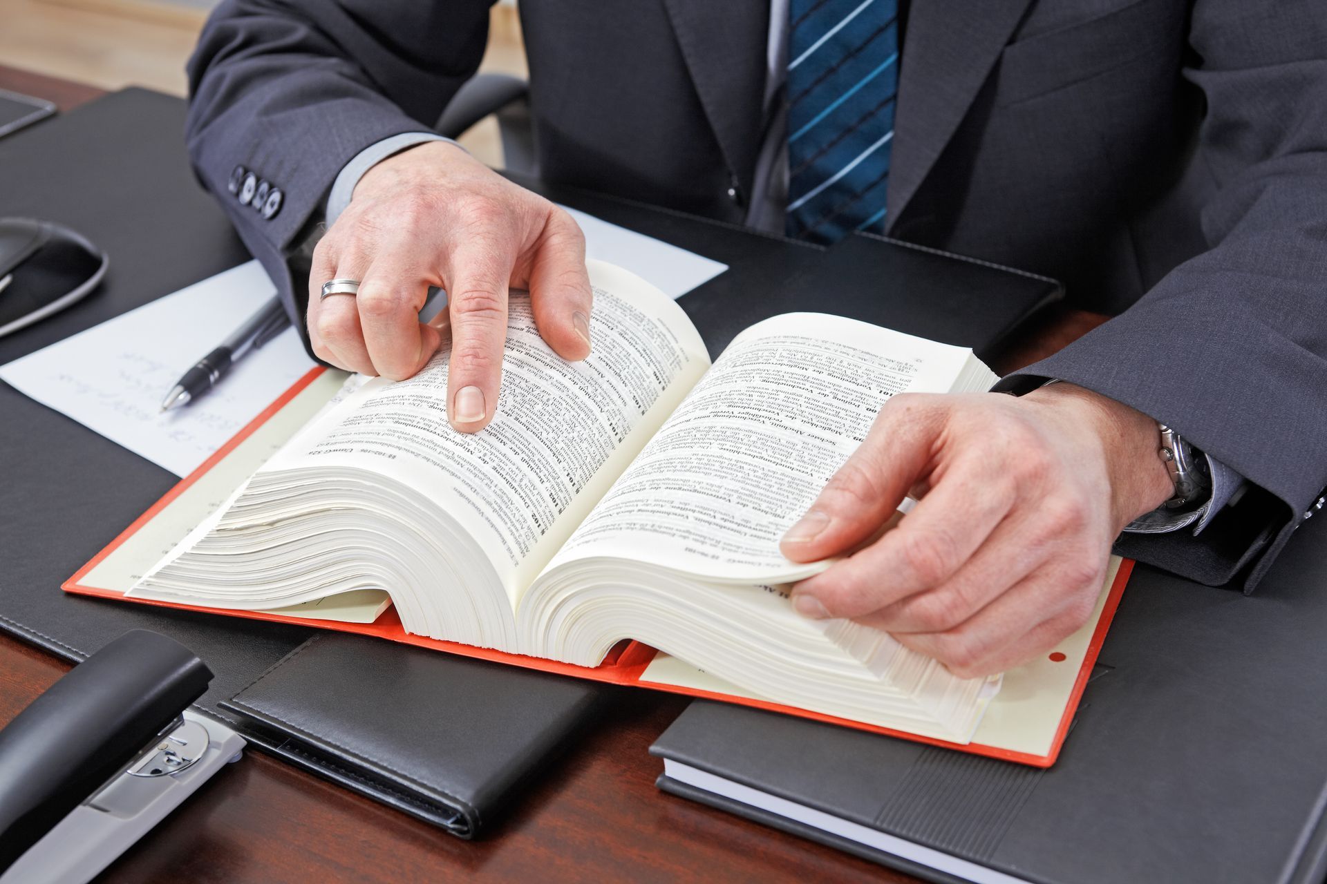 Des mains en costume regarde un livre ouvert sur un bureau.