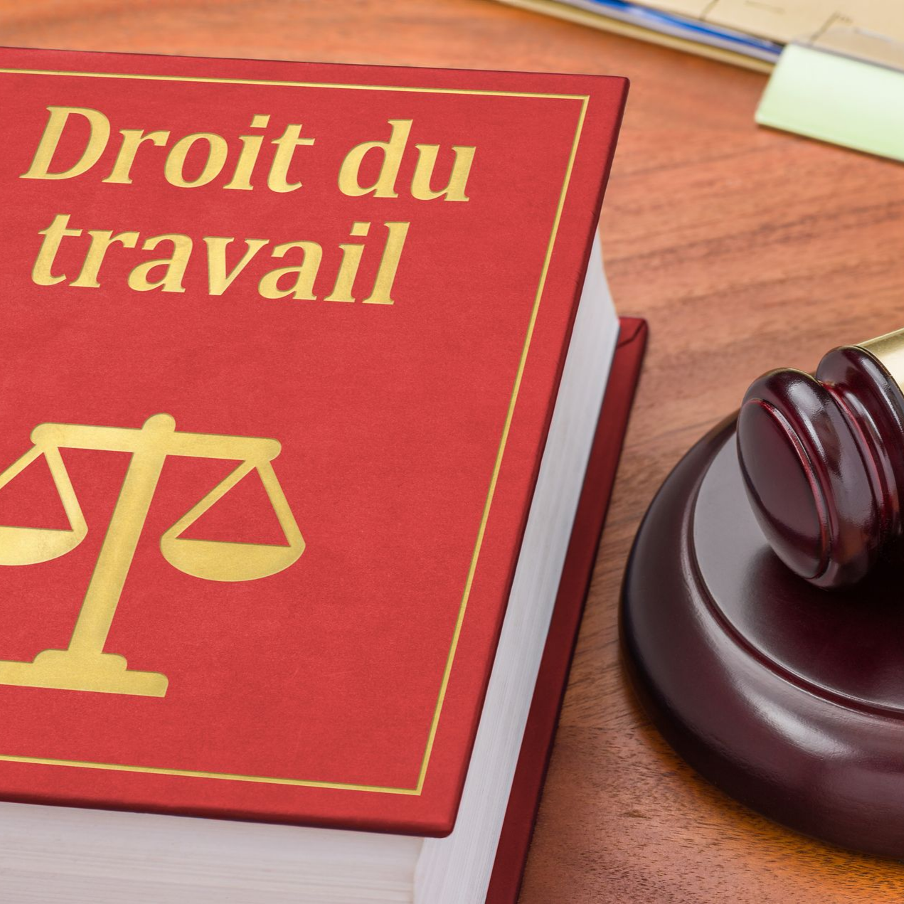 Un livre rouge de droit du travail, posé à côté d'un marteau de juge sur un bureau en bois.