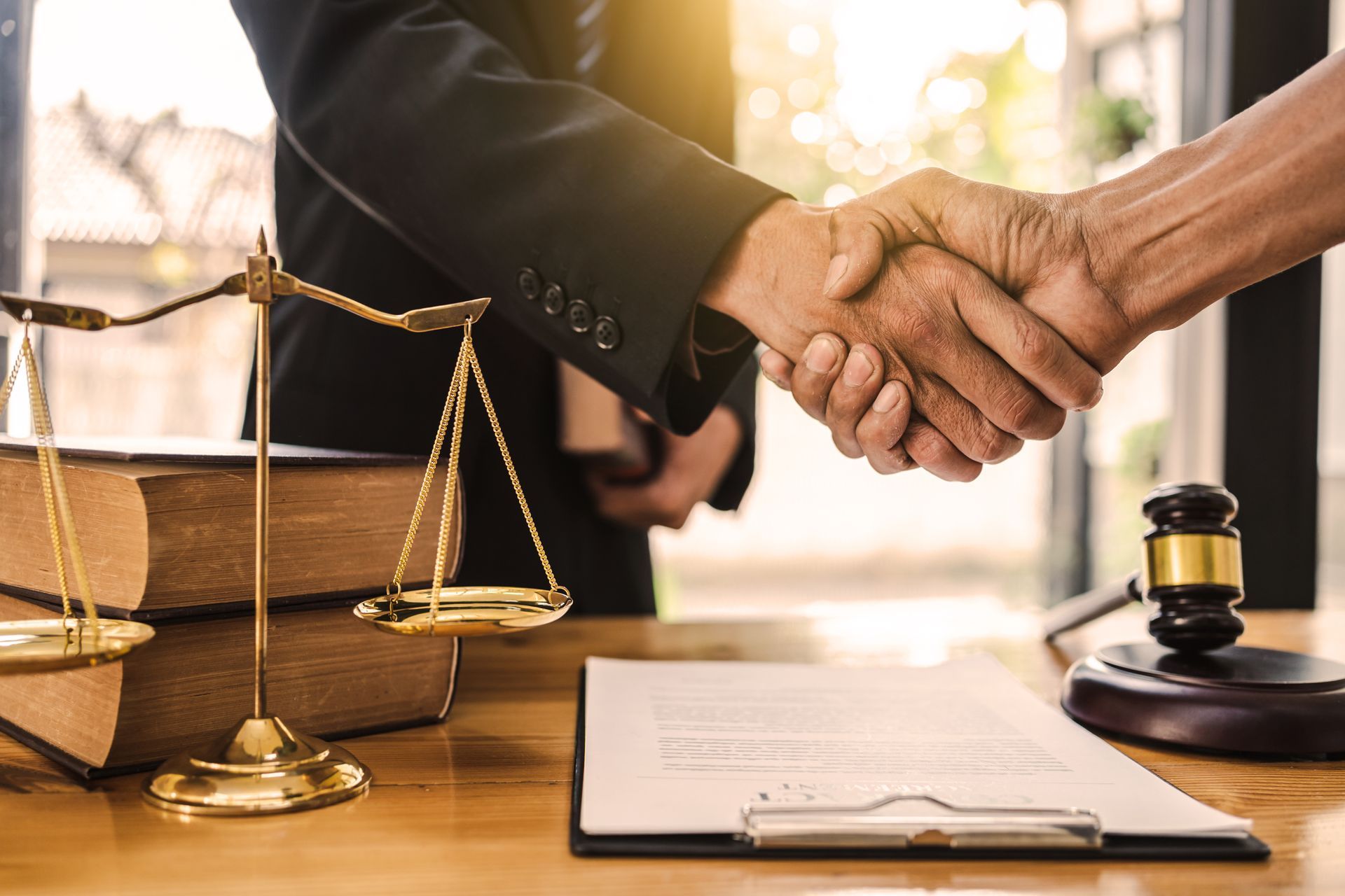 Poignée de main au-dessus du bureau d'un avocat, avec une balance, un maillet et des documents contractuels.