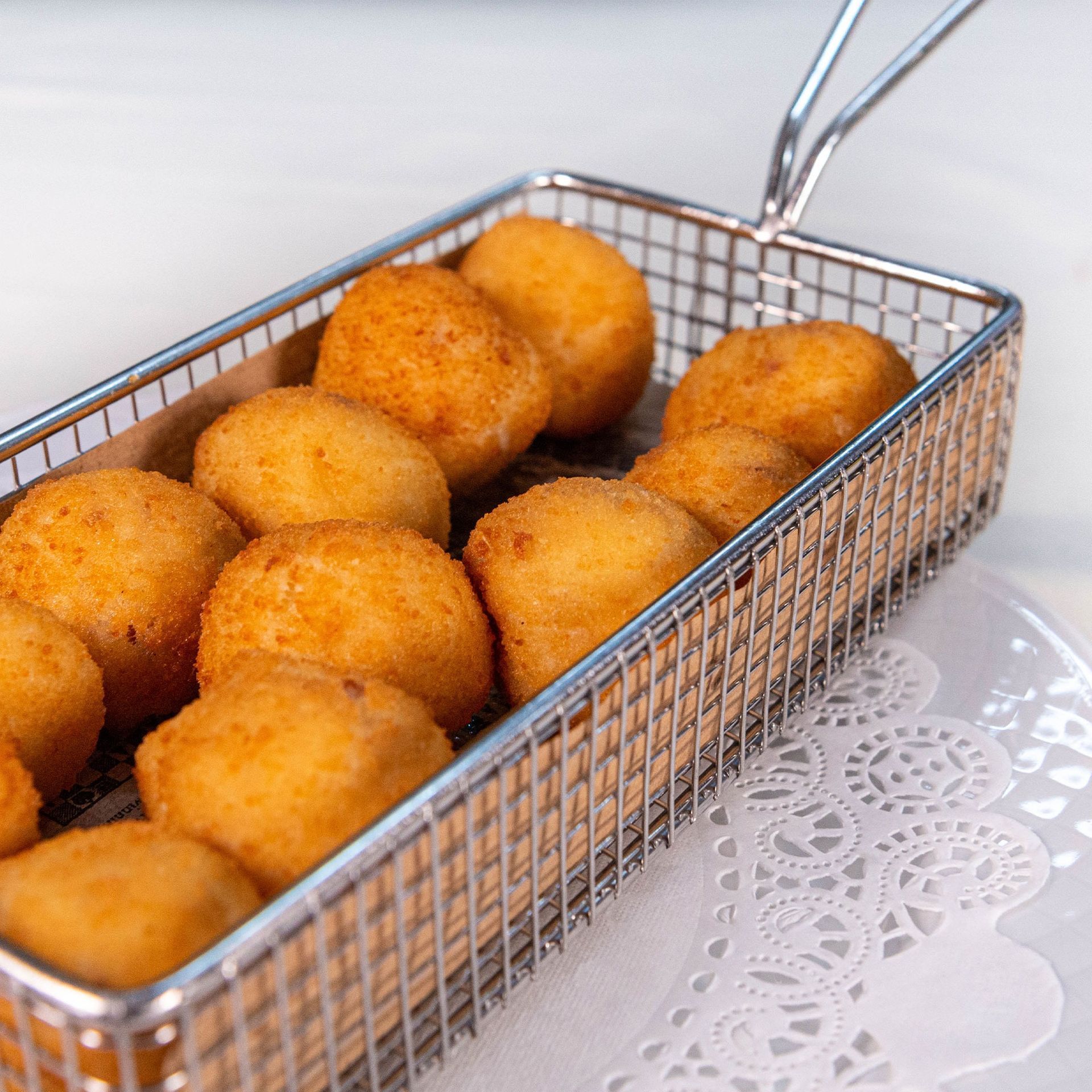 Cesta de bolitas de masa frita doradas sobre un mantel de encaje.