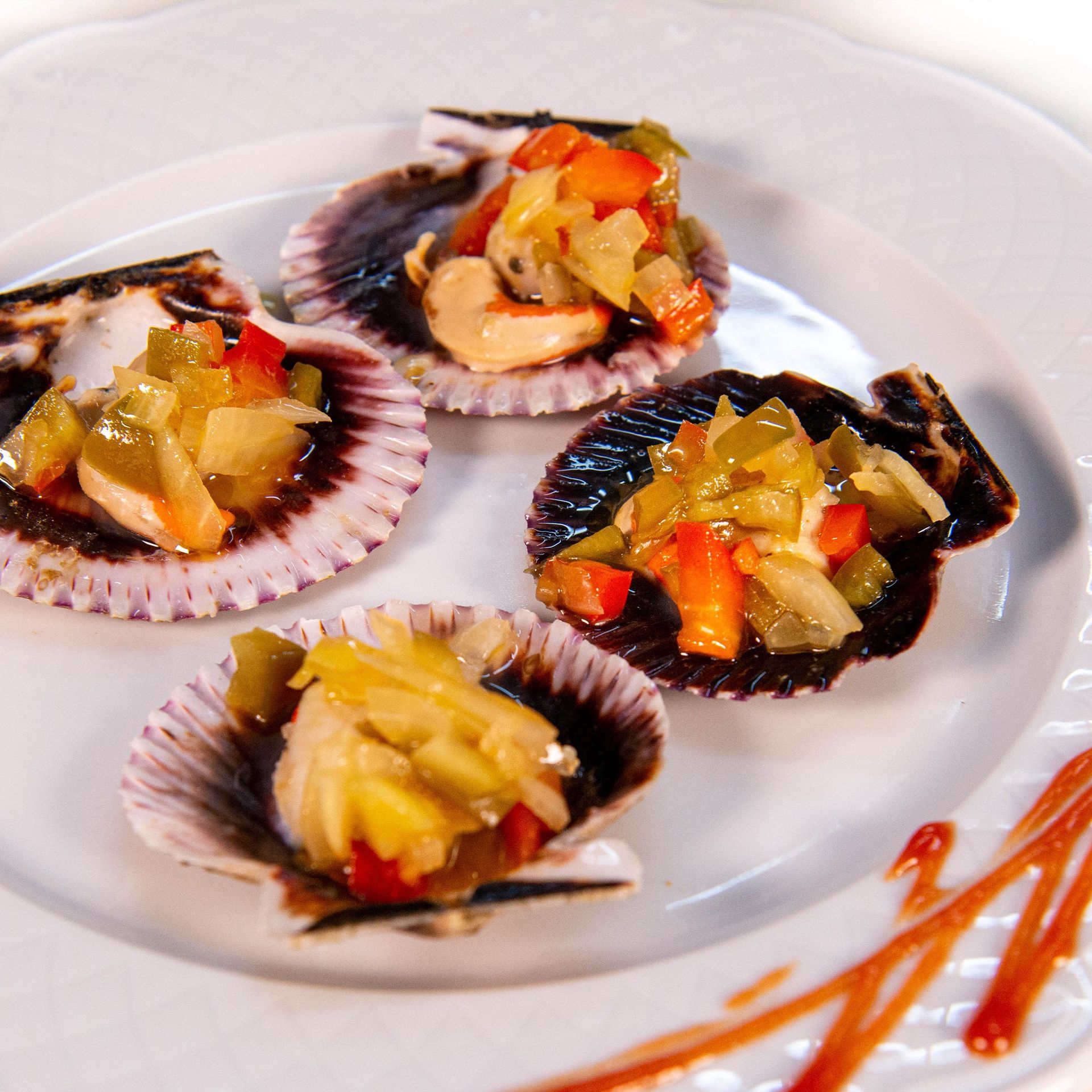 Conchas de vieira rellenas de guarnición de verduras picadas sobre un plato blanco.